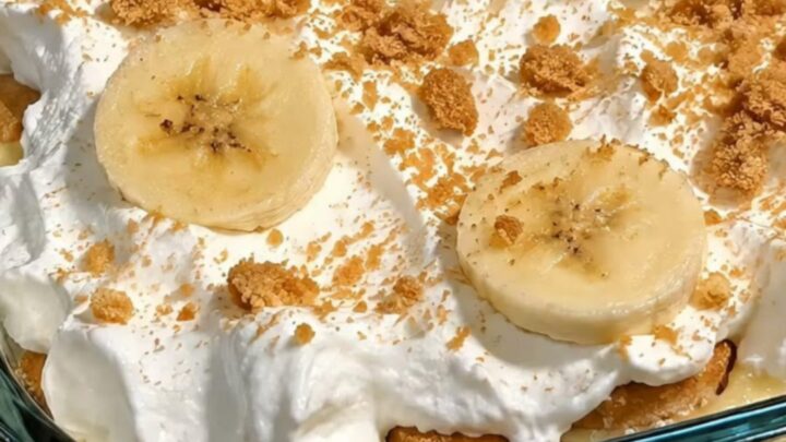 A glass baking dish filled with layers of vanilla custard, sliced bananas, and vanilla wafers topped with whipped cream.