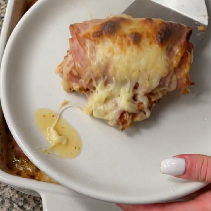 A close-up of a warm, golden-brown ham and cheese roll being lifted with a metal spatula, revealing melted cheese.