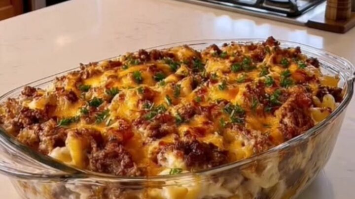 A steaming, bubbly macaroni and beef casserole in a clear glass dish topped with melted cheddar cheese.