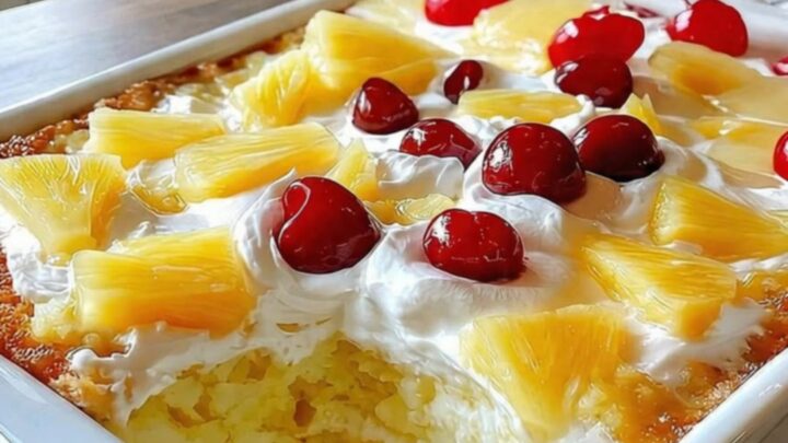 A slice of pineapple paradise cake with whipped cream and a cherry on a white plate.