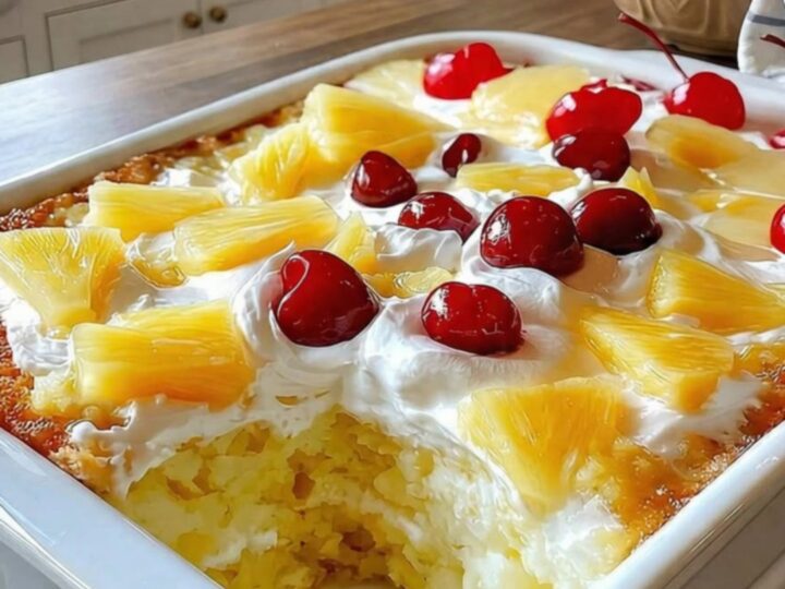 A slice of pineapple paradise cake with whipped cream and a cherry on a white plate.