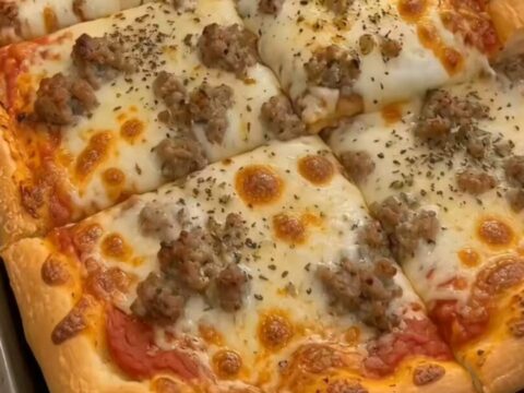 A golden-brown, rectangular sheet pan pizza topped with melted cheese and crumbled sausage.
