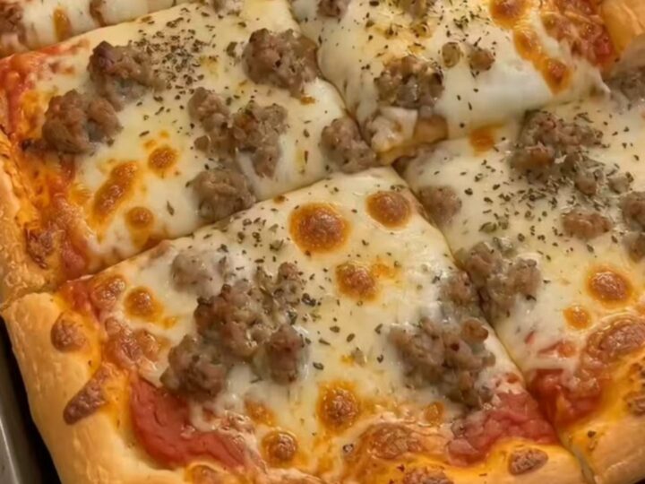 A golden-brown, rectangular sheet pan pizza topped with melted cheese and crumbled sausage.