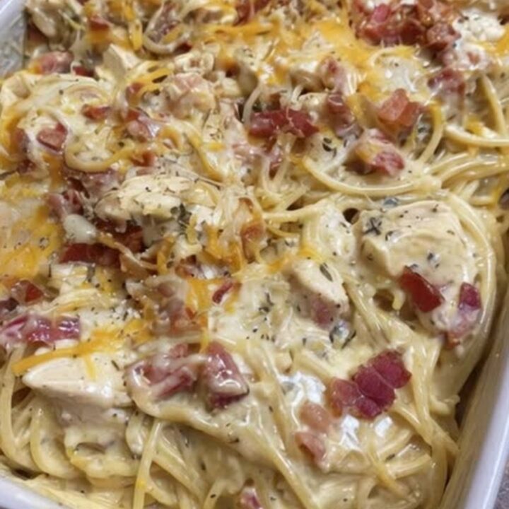 A close-up shot of a fork lifting a creamy, cheesy portion of baked chicken spaghetti topped with bacon bits.