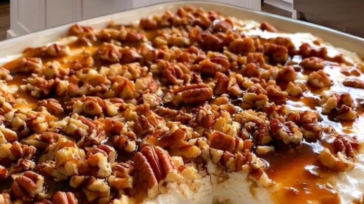 A slice of caramel poke cake with whipped cream and pecans on a white plate.
