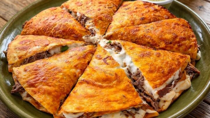 A golden-brown, crispy beef quesadilla slice lifted from an olive-green platter, showing a long, stretchy cheese pull.