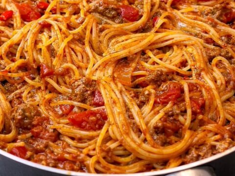 A steaming, glossy heap of spaghetti coated in a rich ground beef tomato sauce served in a black skillet.