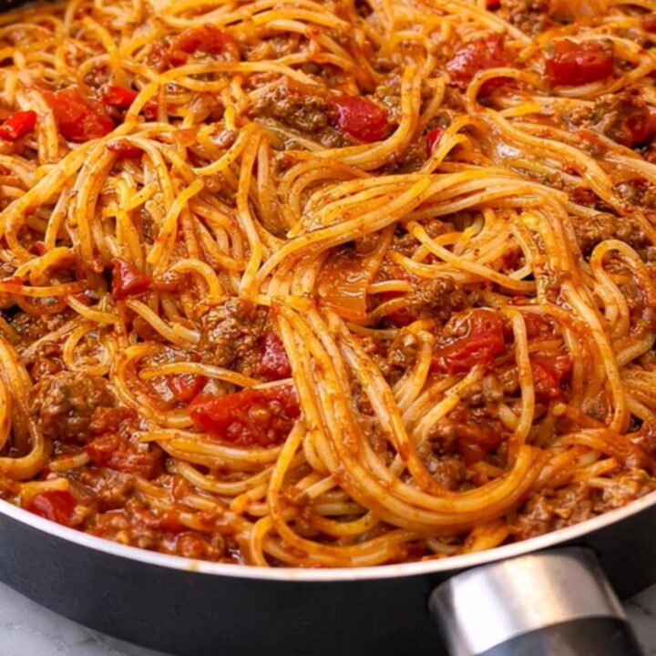 A steaming, glossy heap of spaghetti coated in a rich ground beef tomato sauce served in a black skillet.