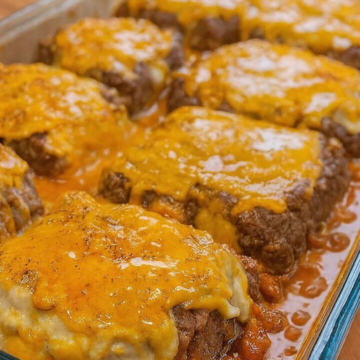 A golden, cheesy Amish hamburger steak bake in a glass dish with a spatula lifting a juicy patty.