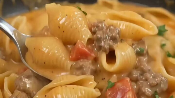 A steaming, creamy beef and mushroom pasta shell dish served in a black skillet.