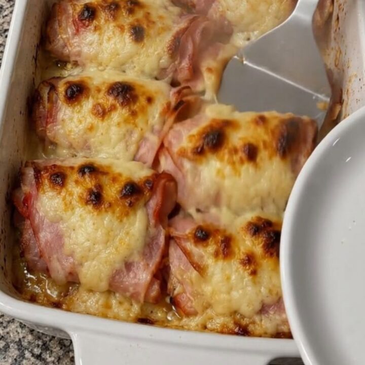 A white ceramic baking dish filled with golden-brown ham and cheese rolls.