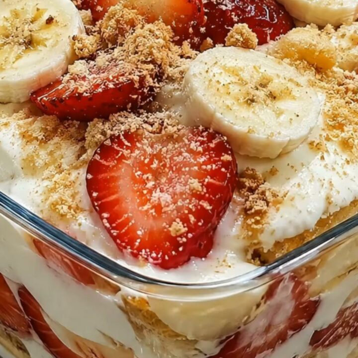 A glass dish filled with layers of creamy banana pudding, sliced strawberries, banana coins, and crushed vanilla wafers.