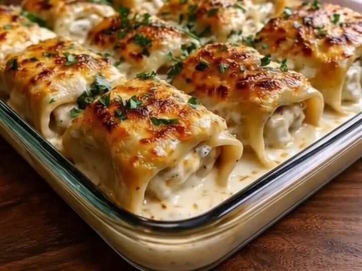 A golden, bubbly chicken alfredo lasagna roll being lifted from a baking dish with a spatula.