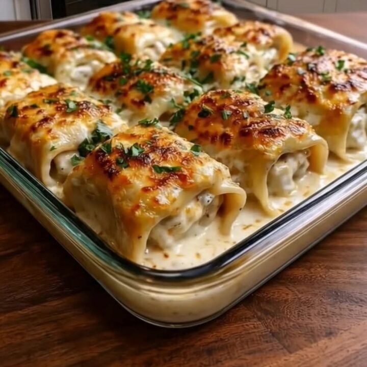 A golden, bubbly chicken alfredo lasagna roll being lifted from a baking dish with a spatula.