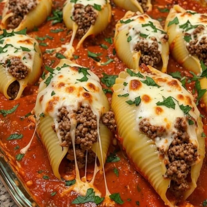 A glass baking dish filled with meat-stuffed jumbo shells covered in melted cheese and garnished with parsley.