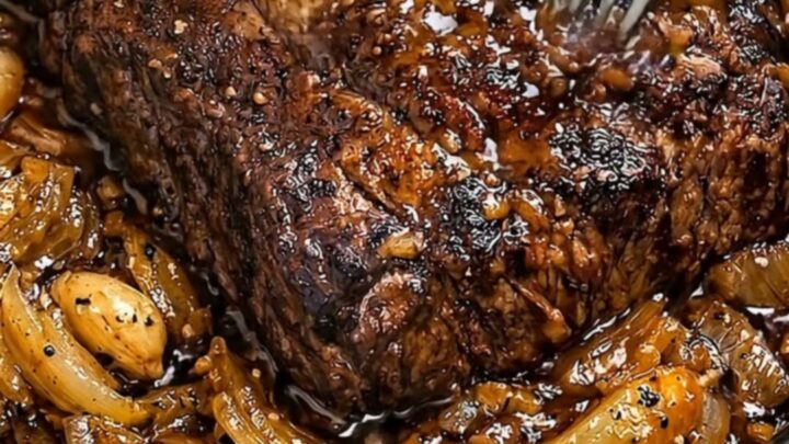 A steaming, tender beef pot roast topped with rich, caramelized onions in a black slow cooker.
