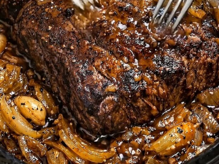 A steaming, tender beef pot roast topped with rich, caramelized onions in a black slow cooker.
