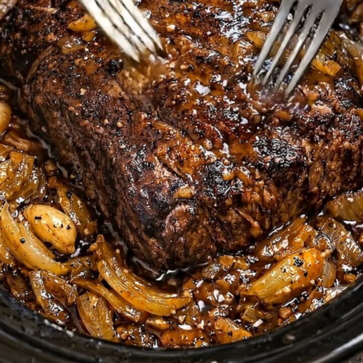 A steaming, tender beef pot roast topped with rich, caramelized onions in a black slow cooker.