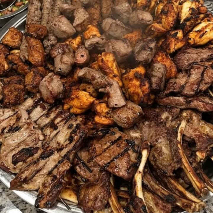 A large metal platter filled with perfectly charred lamb chops and savory meat kebabs.