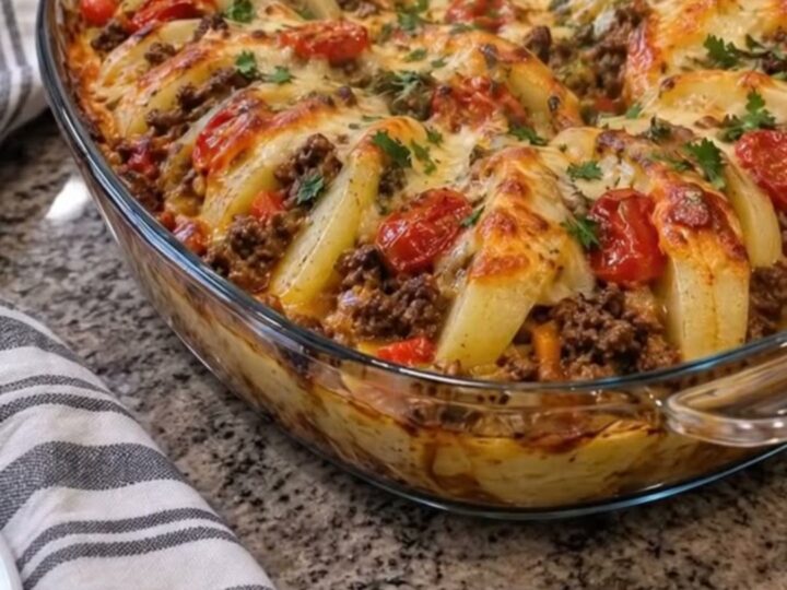 A steaming cheesy potato and ground beef casserole in an oval glass baking dish on a granite counter.