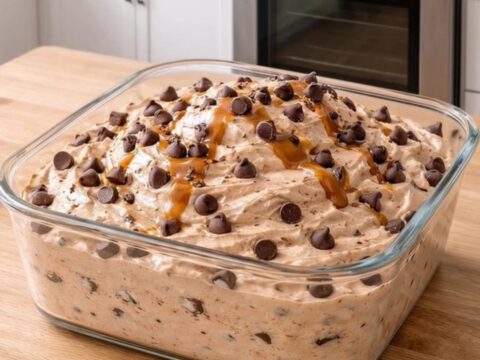 Square glass dish holding creamy peanut butter fluff loaded with chocolate chips and caramel drizzle.