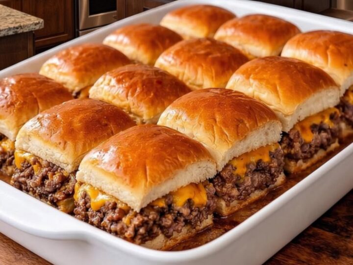 A close-up of golden-brown cheeseburger sliders in a white baking dish with melted cheese.