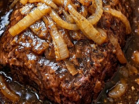 A succulent slow cooker pot roast topped with caramelized onions on a white serving platter.