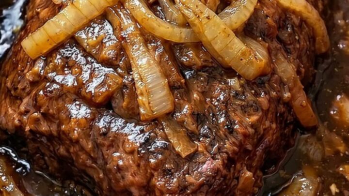 A succulent slow cooker pot roast topped with caramelized onions on a white serving platter.