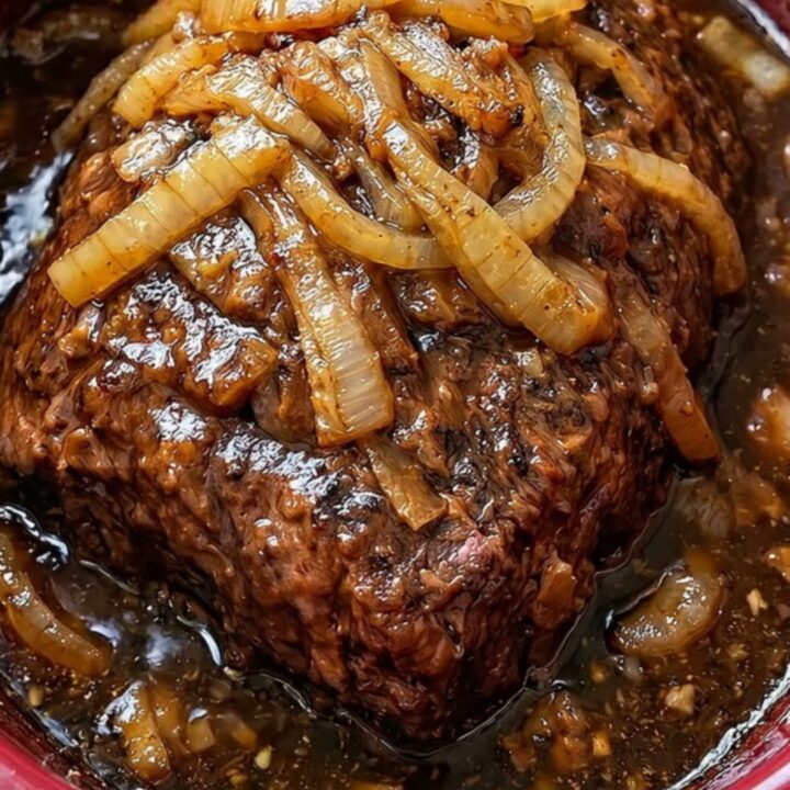 A succulent slow cooker pot roast topped with caramelized onions on a white serving platter.