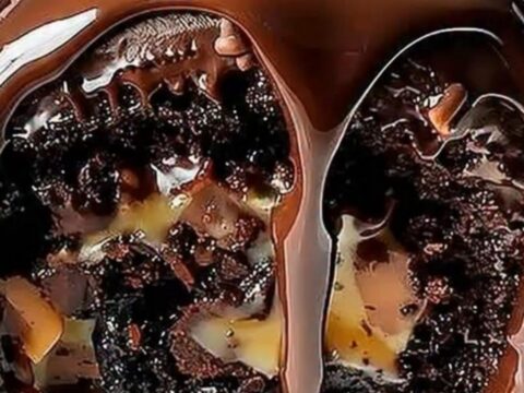 A glossy chocolate-glazed cake roll topped with pecans sitting on a white serving platter.