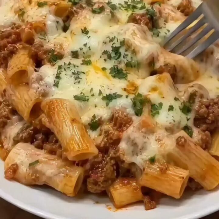 A steaming, freshly baked beef rigatoni pasta in a ceramic dish, topped with golden melted cheese and fresh parsley.