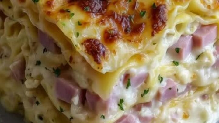A tall square slice of lasagna with distinct layers of pasta, ham cubes