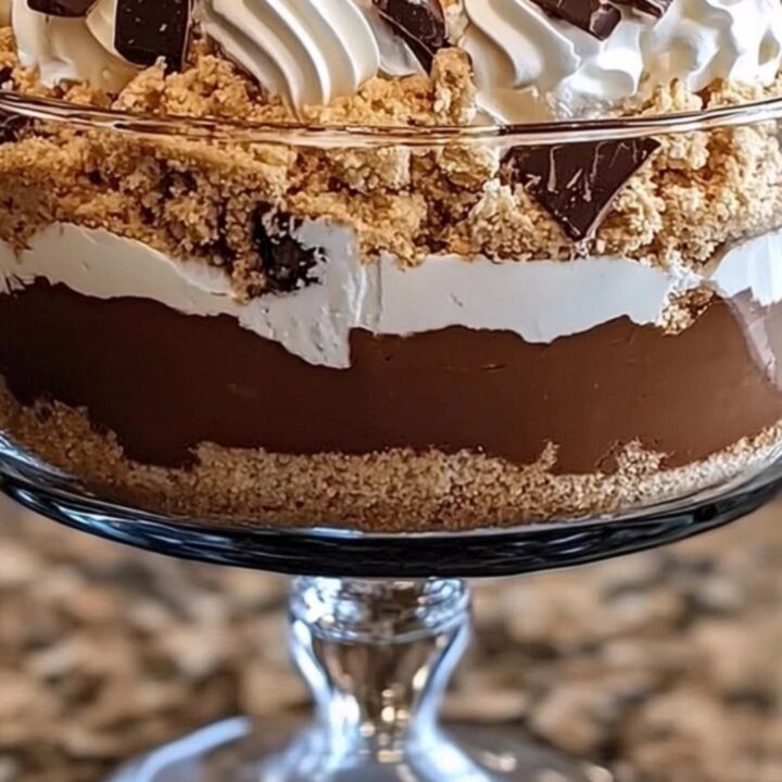 A glass trifle dish filled with beautiful, distinct layers of chocolate pudding, cream, and graham cracker crumbs.
