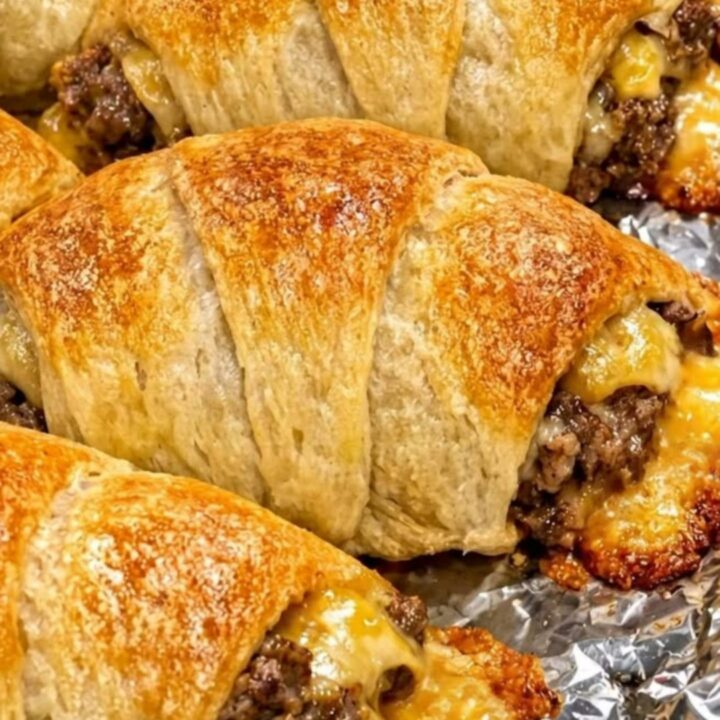 Golden, flaky crescent rolls arranged on a baking sheet, filled with seasoned beef and melted cheese.