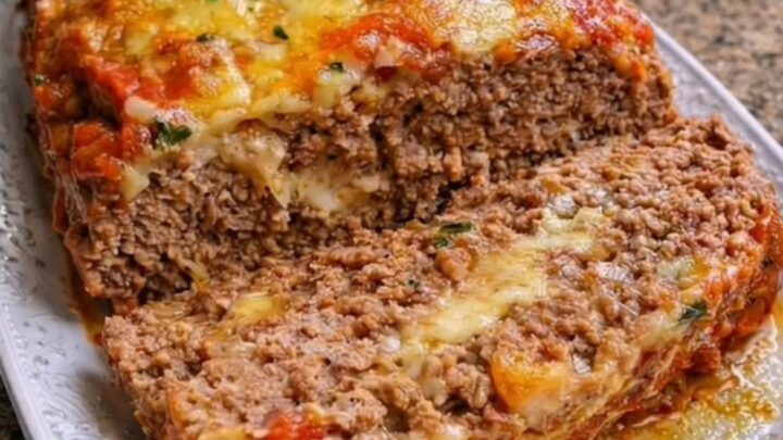 Golden-baked meatloaf on a white platter topped with marinara sauce and melted mozzarella cheese.