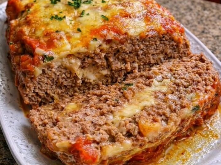 Golden-baked meatloaf on a white platter topped with marinara sauce and melted mozzarella cheese.