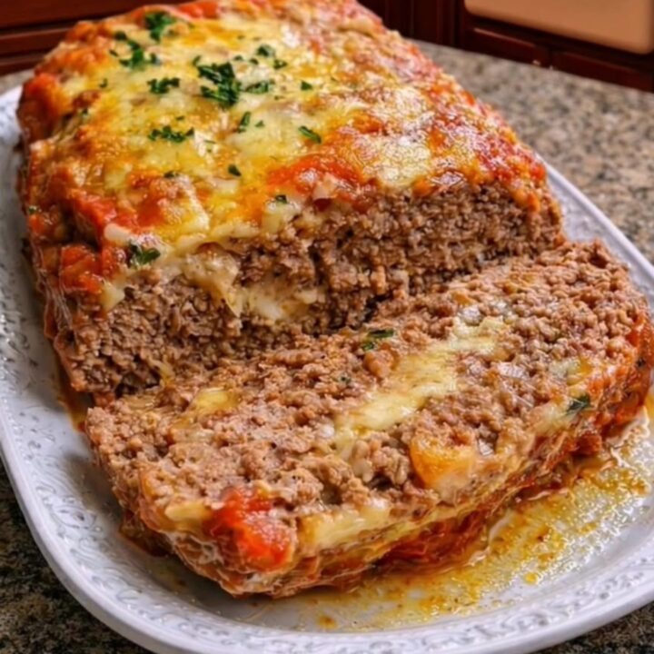 Golden-baked meatloaf on a white platter topped with marinara sauce and melted mozzarella cheese.