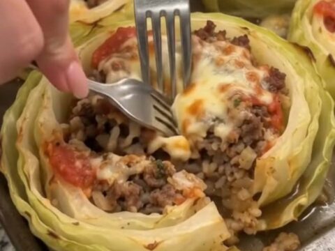 A close-up shot of a baked cabbage ring stuffed with seasoned ground beef, topped with melted