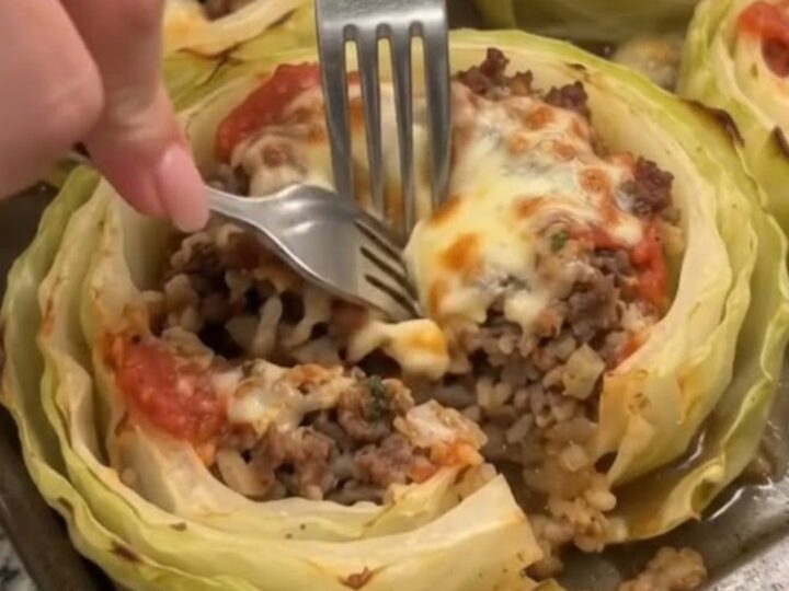 A close-up shot of a baked cabbage ring stuffed with seasoned ground beef, topped with melted