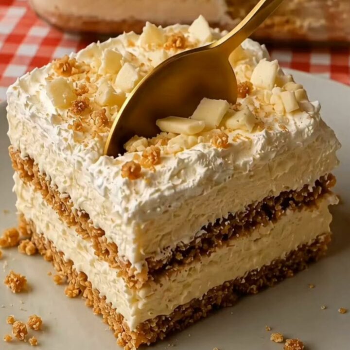 A neat square of white chocolate biscuit cake sitting on a white plate with visible creamy layers.