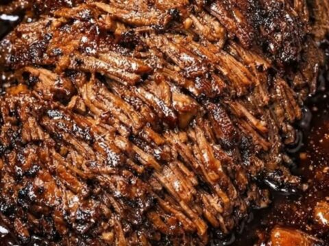 A close-up view of succulent, fork-tender shredded beef roast served on a white ceramic plate with visible steam.