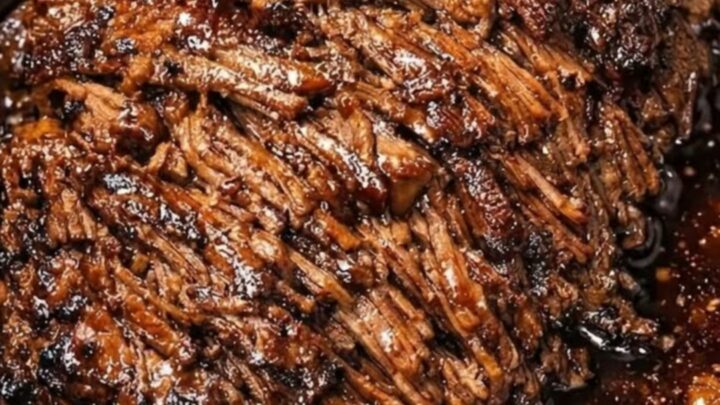 A close-up view of succulent, fork-tender shredded beef roast served on a white ceramic plate with visible steam.