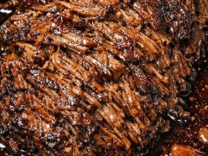 A close-up view of succulent, fork-tender shredded beef roast served on a white ceramic plate with visible steam.