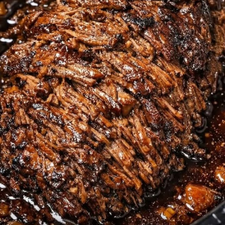 A close-up view of succulent, fork-tender shredded beef roast served on a white ceramic plate with visible steam.