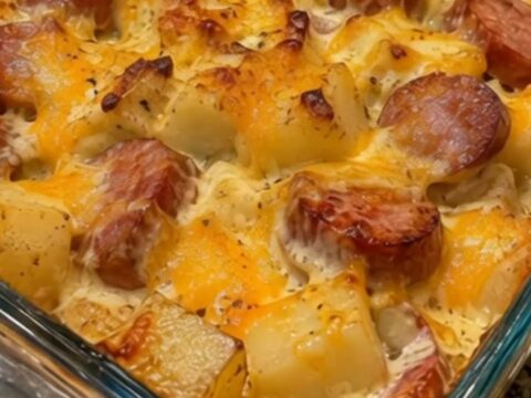 A close-up of a creamy loaded sausage and potato bake in a glass dish with melted cheese.