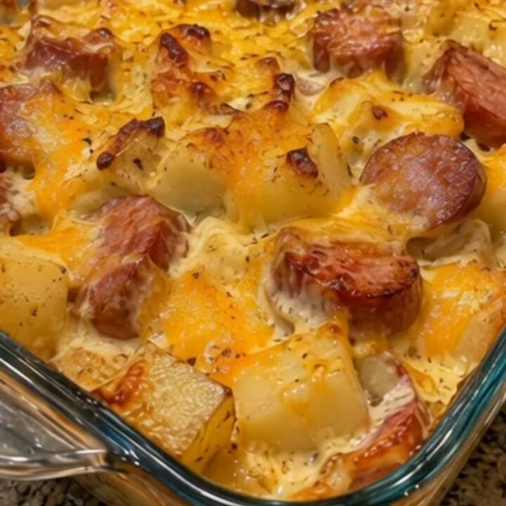 A close-up of a creamy loaded sausage and potato bake in a glass dish with melted cheese.