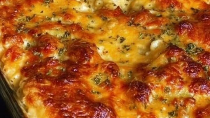 A close-up of a creamy baked macaroni and cheese in a glass dish with a golden herb crust.