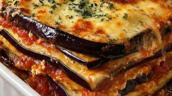 A steaming portion of eggplant lasagna with layers of tomato sauce and melted cheese in a white ceramic dish.