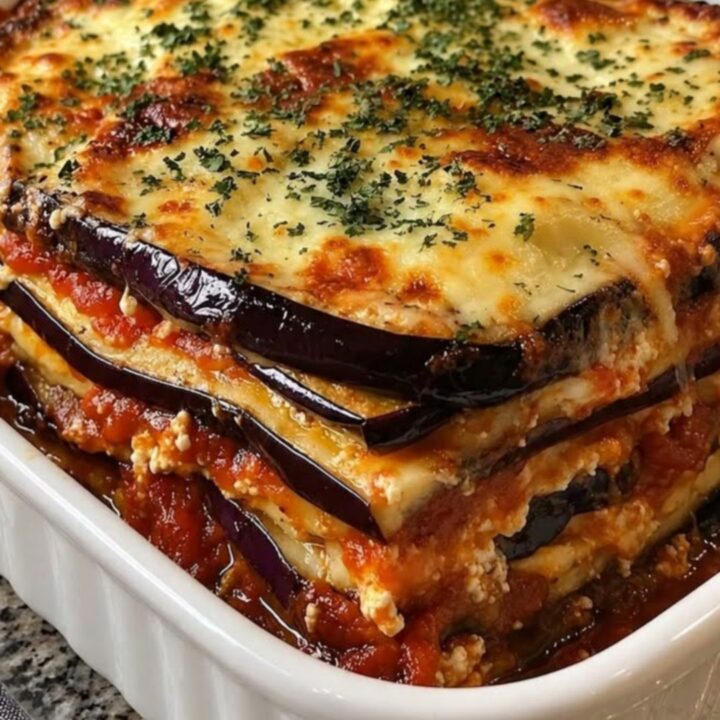 A steaming portion of eggplant lasagna with layers of tomato sauce and melted cheese in a white ceramic dish.