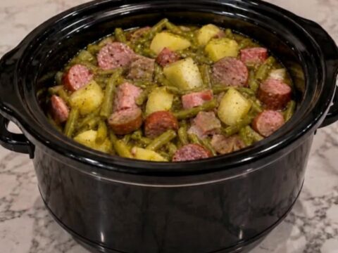 A steaming bowl of slow-cooked green beans, potato chunks, and sliced smoked sausage.